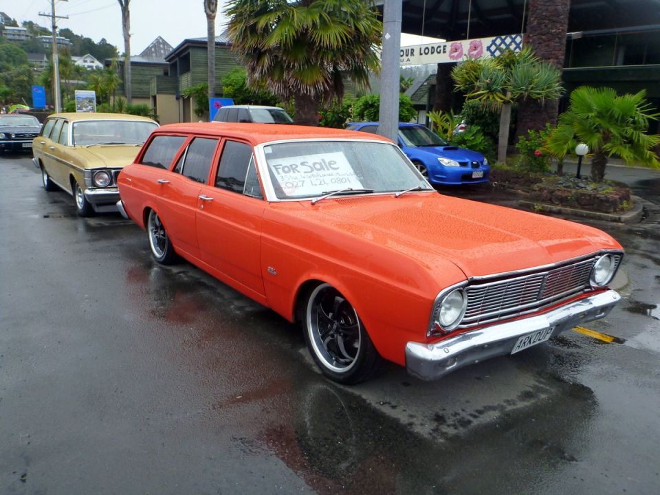 Orange station wagon with a "For Sale" sign parked on a wet street.