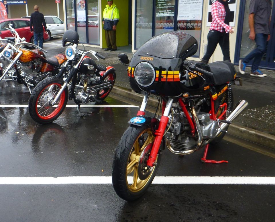 Two custom motorcycles parked on a wet street.
