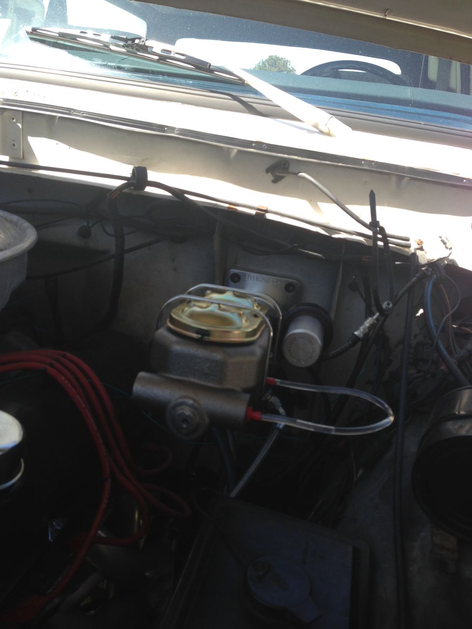 Close-up of a vehicle's brake master cylinder with gold cap and clear fluid lines.