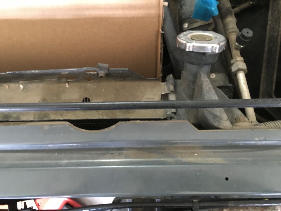 Close-up of a vehicle's radiator cap and surrounding engine parts with a cardboard box above.