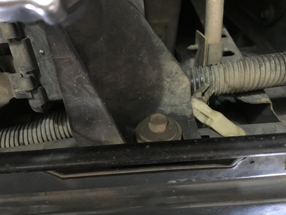 Close-up of a rusted bolt and broken clip on a conduit in an engine bay.