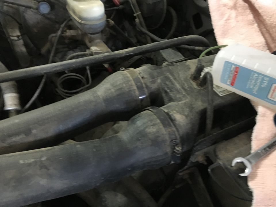 Engine bay of a 1987 Ford Bronco with hoses and a bottle of isopropyl alcohol.