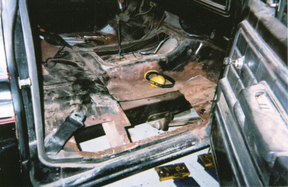 Stripped truck cab interior with rusted floor pan cut open during restoration