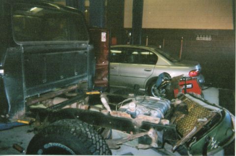 1978 Ford Bronco - Garage scene with a truck chassis and a silver sedan parked behind it.