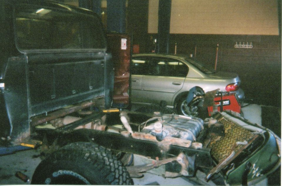 Truck chassis in foreground, silver sedan in background in garage