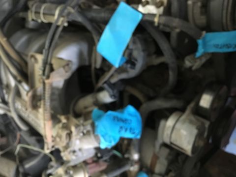 1987 Ford Bronco - Close-up view of an engine bay with blue tape marking various components. The engine appears to be from a Ford Bronco, with hoses, wires, a…