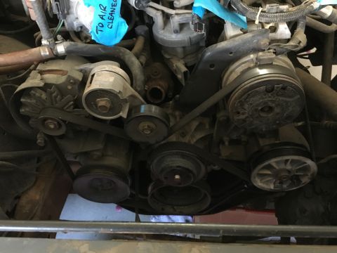 1987 Ford Bronco - This is a close-up, low-angle shot of the engine bay of a 1987 Ford Bronco. Multiple belts and pulleys are visible, including the alternato…
