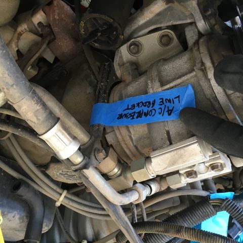 1987 Ford Bronco - A close-up view of an engine bay shows an A/C compressor with a blue tape label that reads "A/C COMPRESSOR LINE BRACKET".