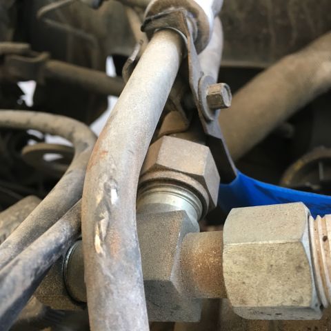 1987 Ford Bronco - A close-up view of metal hydraulic lines and fittings, likely from an engine bay, covered in dust and grime. A blue handle is visible on on…