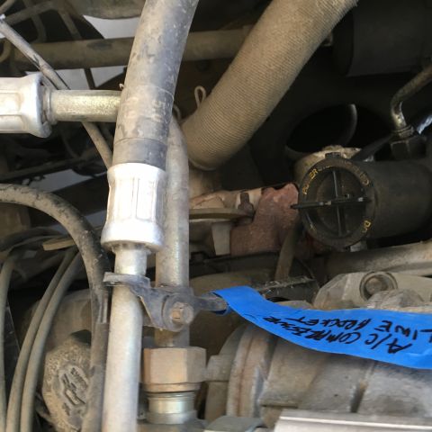 1987 Ford Bronco - A close-up view of automotive engine components, including hoses and a reservoir with text. Blue tape with handwritten text is visible acro…