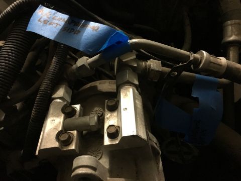 1987 Ford Bronco - Blue tape with handwritten notes is applied to metal components and hoses in a vehicle's engine bay. One piece of tape reads "LEFT SIDE".