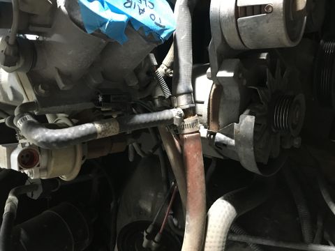 1987 Ford Bronco - A close-up view of engine components in a 1987 Ford Bronco, including hoses, an alternator, and part of the intake manifold.