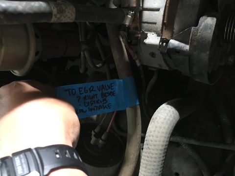 1987 Ford Bronco - A blue piece of tape with handwritten instructions is attached to engine components. The text reads "TO EGR VALVE ? RIGHT BESIDE . DISTRIB…