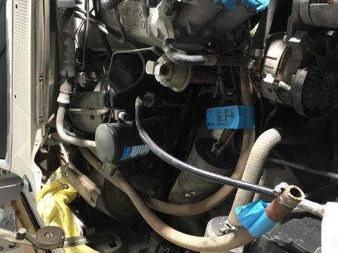 1987 Ford Bronco - A close-up view of a vehicle's engine bay, showing various hoses, components, and a blue taped label with handwritten text. The label reads…