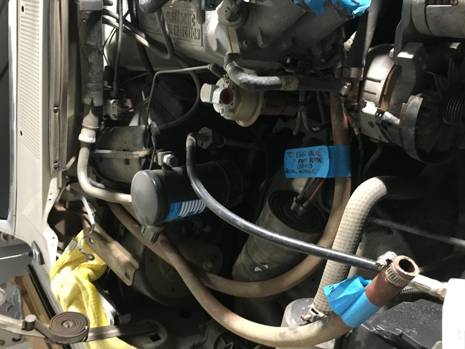 Vehicle engine bay with hoses and a blue taped label.