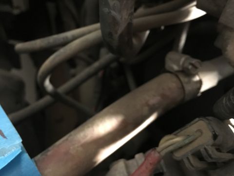 1987 Ford Bronco - A close-up view of a section of an engine bay, showing various hoses, pipes, and electrical connectors. A metal pipe with a clamp is promin…