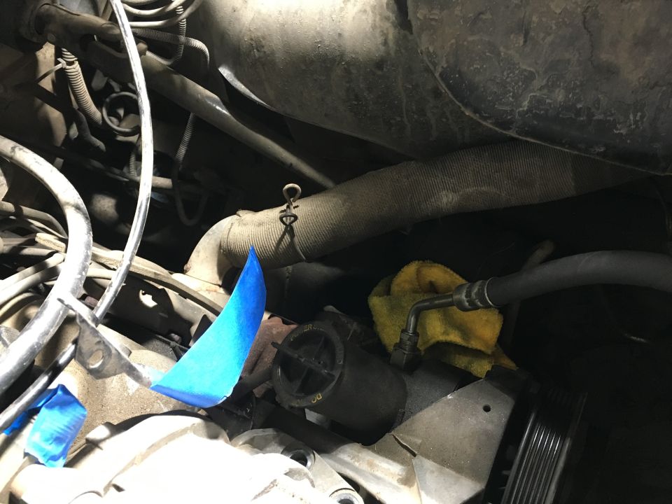 Engine bay with power steering hose, yellow rag, and blue tape on bracket.