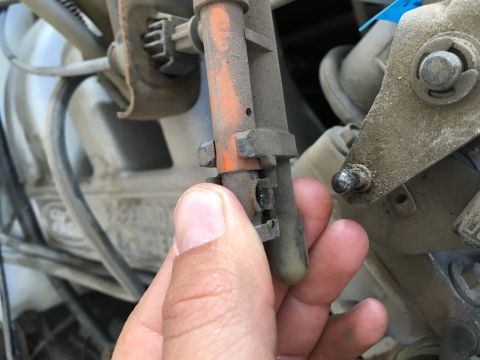 1987 Ford Bronco - A hand holds a dusty, orange and gray electrical connector with visible damage to its housing. The connector is part of a vehicle's engine…