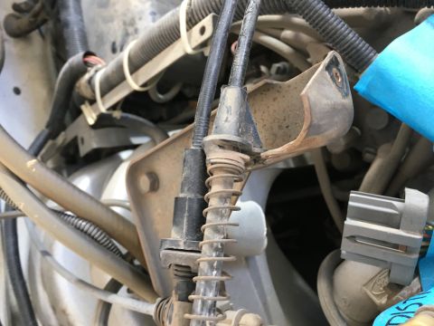 1987 Ford Bronco - A close-up view of engine bay components in a 1987 Ford Bronco, showing various cables, hoses, and a broken metal bracket.