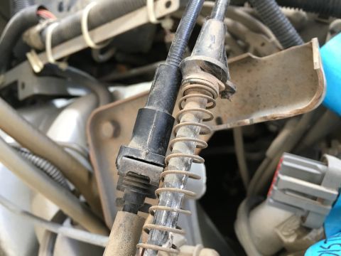 1987 Ford Bronco - A close-up view shows two cables with springs and plastic housings, likely from a vehicle's engine bay. The cables are dusty and show signs…