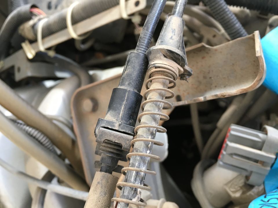 Close-up of two dusty cables with springs in a vehicle engine bay.