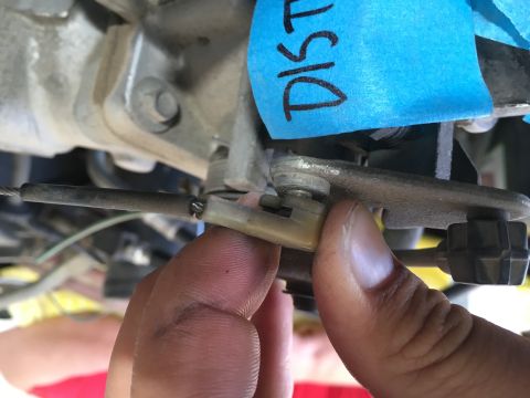 1987 Ford Bronco - A close-up view shows a hand holding a cable connected to a linkage mechanism. Blue tape with the word "DIST" is visible in the background.