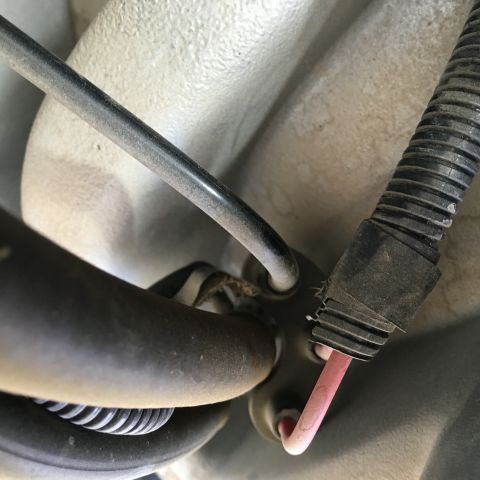 1987 Ford Bronco - A close-up view shows a pink wire emerging from a black corrugated conduit attached to a vehicle's undercarriage. Another dark-colored tube…