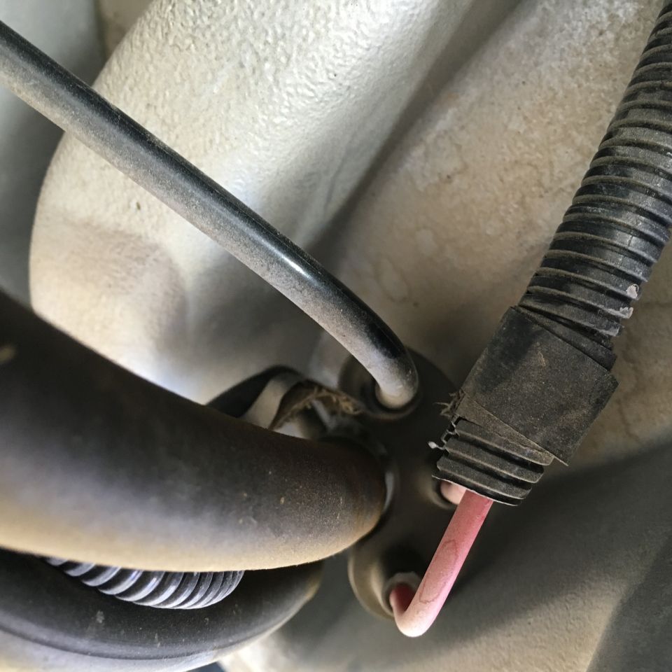 Close-up of a pink wire exiting a black conduit on a vehicle's undercarriage.