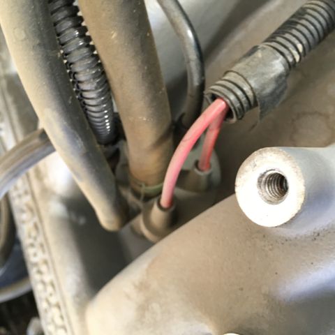 1987 Ford Bronco - A close-up view shows red electrical wires emerging from a black corrugated conduit, connected to a sensor or component. A threaded metal b…