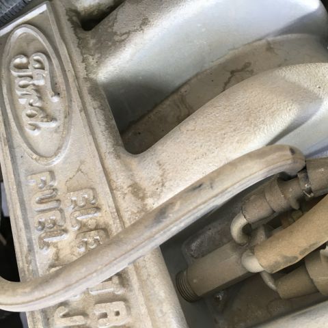 1987 Ford Bronco - A close-up view of a dusty Ford fuel injection manifold with the Ford logo embossed on the side. Visible text includes "FUEL" and "INJ."