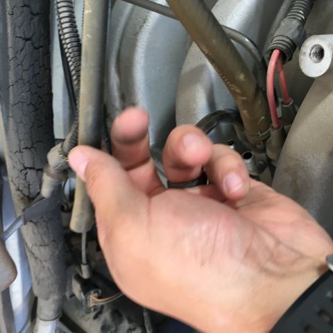 1987 Ford Bronco - A hand is shown reaching towards various hoses and wires connected to an engine component. The background appears to be the engine bay of a…