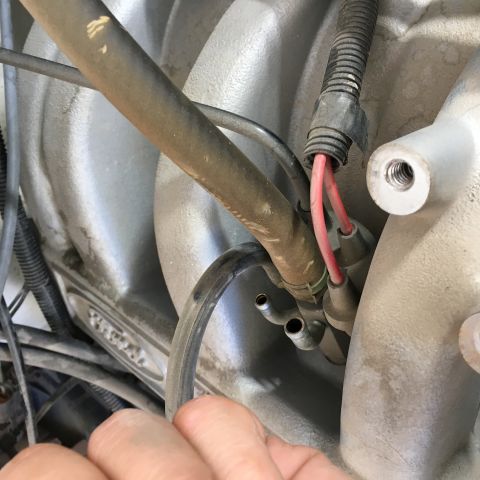 1987 Ford Bronco - A close-up view of engine components, including hoses and wiring connected to a silver intake manifold. A hand is visible in the foreground…