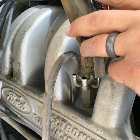 1987 Ford Bronco - A close-up view shows a hand with a gray ring touching a metal component on a dusty Ford engine. The component appears to be part of the fu…