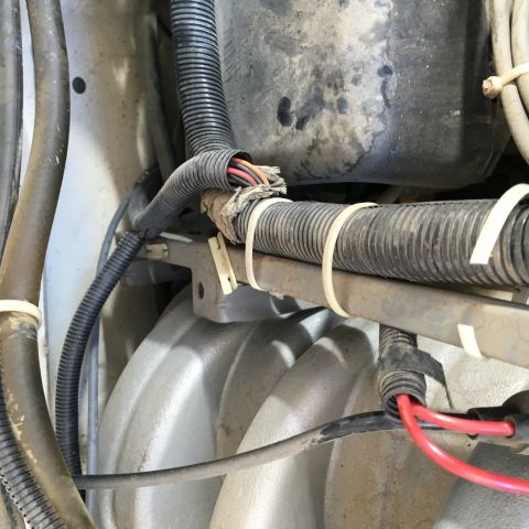 1987 Ford Bronco - A close-up view shows damaged wiring harness with exposed wires, secured by zip ties to a metal bracket above an engine component.