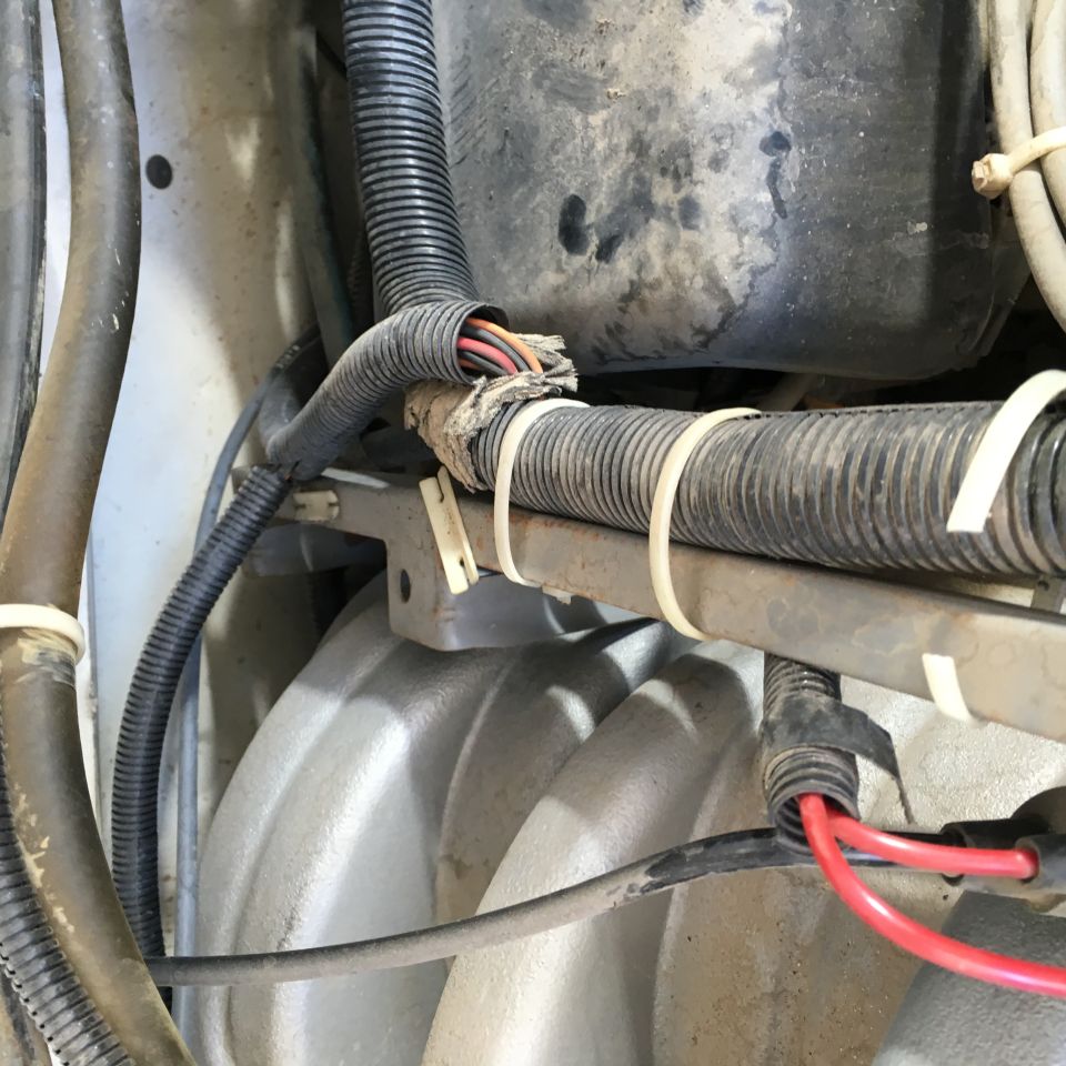 Damaged wiring harness with exposed wires secured by zip ties to a bracket.