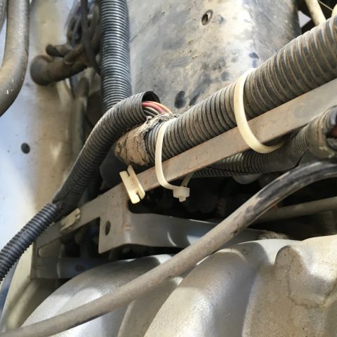 1987 Ford Bronco - A close-up view of wiring harnesses and conduits secured with zip ties and tape to a metal bracket in an engine bay. The components appear…