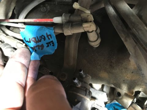 1987 Ford Bronco - A hand is holding a piece of blue tape with handwritten text that reads "E/F 4 bottom" over a section of engine components. The tape is obs…