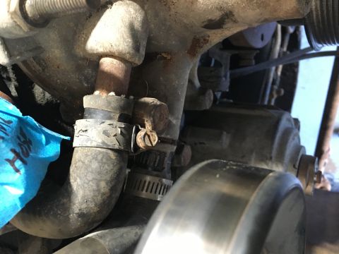 1987 Ford Bronco - A close-up view of a rusty metal pipe connected to a rubber hose with a metal clamp on a vehicle engine. The hose is dark gray and appears…