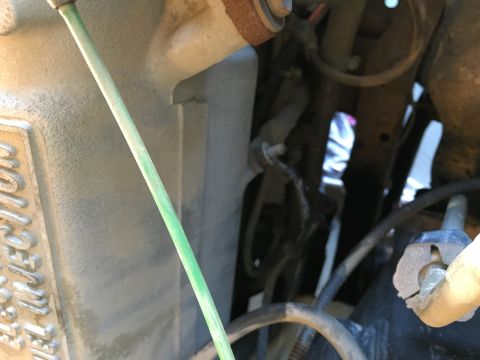 1987 Ford Bronco - A close-up view of a green cable running alongside a dusty, metallic engine component with embossed text that reads "FUEL INJECTION".