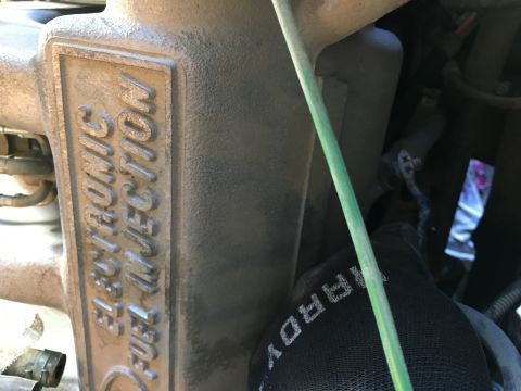 1987 Ford Bronco - A close-up view of the intake manifold on a vehicle, which is embossed with the words "ELECTRONIC FUEL INJECTION". A green wire and a glove…