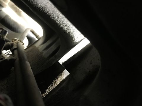1987 Ford Bronco - A close-up view of a metal bracket with a sharp, angled edge, illuminated by a bright light source. Dust and grime cover the surrounding en…