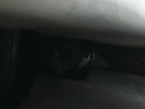 1987 Ford Bronco - A close-up, dimly lit shot shows a dark-colored bolt head with some wear and tear. The bolt appears to be recessed into a dark metal surfac…