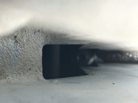 1987 Ford Bronco - A close-up view of a dark, recessed opening in a textured, light-colored vehicle component. A small, dark object with a circular opening is…