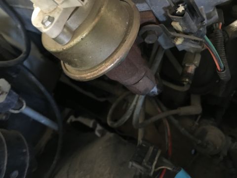 1987 Ford Bronco - A close-up view of engine components in a vehicle, including a metal diaphragm actuator with a copper-colored rim and various hoses and ele…
