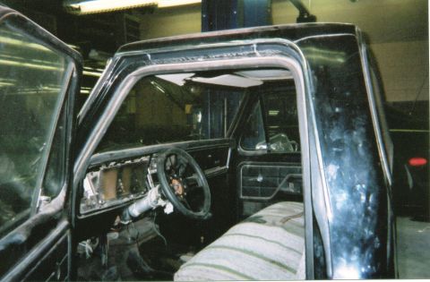 1978 Ford Bronco - The interior of a black pickup truck shows a torn headliner, an aftermarket steering wheel, and a partially disassembled dashboard.