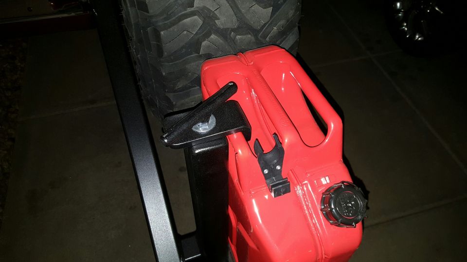 Red jerry can mounted to a vehicle with a large off-road tire in the background.