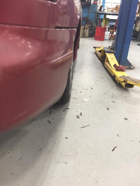 1995 Ford Probe - Side view of the rear quarter panel and tire of a red car, parked in a garage near a yellow car lift.