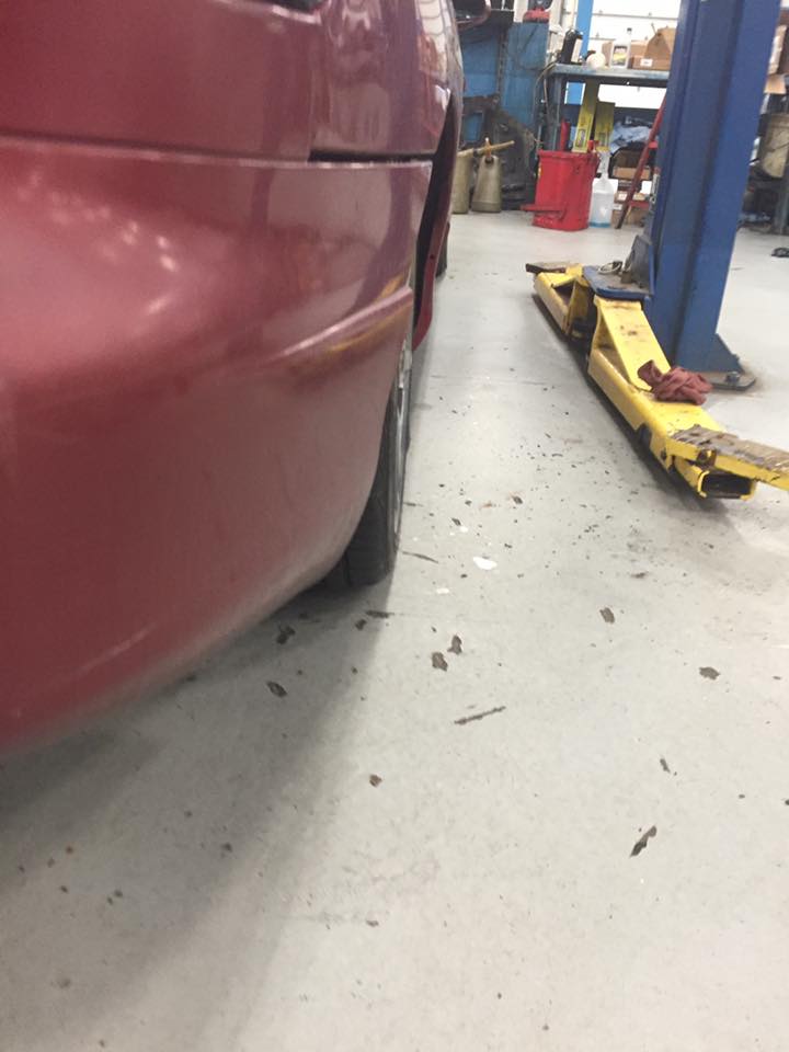 Red car rear quarter panel and tire next to a yellow car lift in a garage.