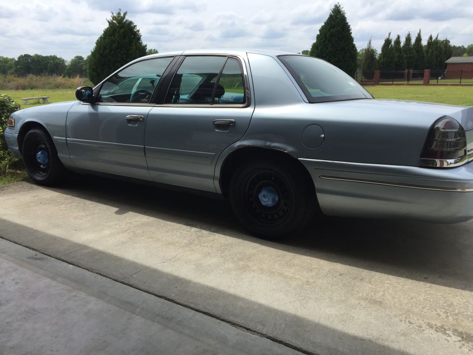 Light blue sedan parked on concrete driveway, rear driver's side view.