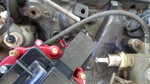 1978 Ford Bronco - A close-up view of a black ignition coil with red accents and brass terminals, mounted on a dark-colored engine block. Text on the coil rea…